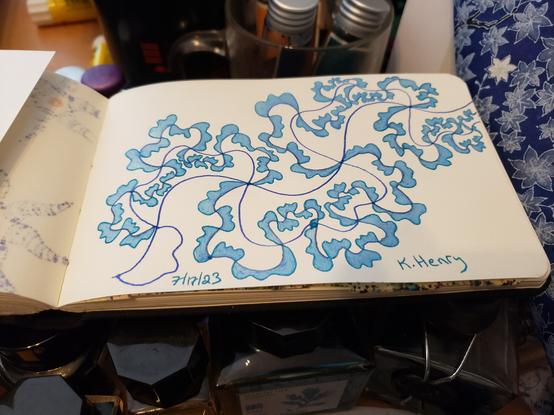 Hand drawn generative art in ink on an open page of my sketchbook. The pattern is an abstract fractal ruffle, and the sketchbook is sitting on top of bottles of ink.