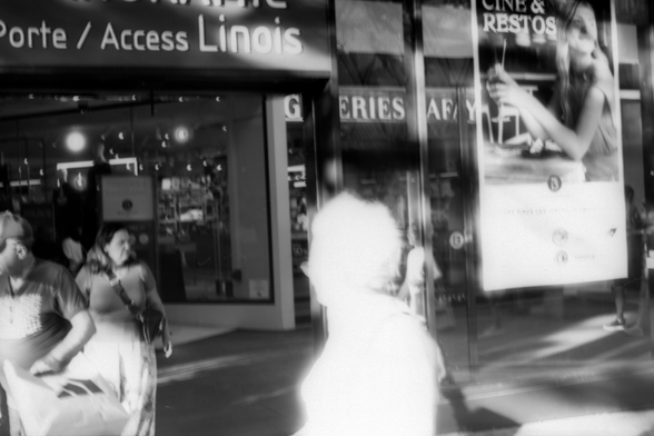 A black and white photograph of a street in Paris in the 15th arrondissement. It is a high contrast scene. A figure walks in front of the frame and is completely white as the highlight are blown out, much in the style of Australian photographer Trent Parke.