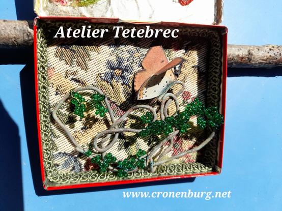 The lower part: A butterfly sits on a randomly curved thick wire. It has tiny leaves made with glass rocailles. The background is a floral vintage tapestry, framed with braids.