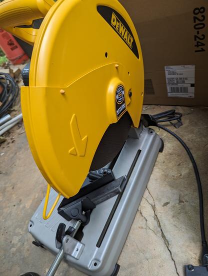 A Dewalt chop saw on the concrete floor ready to cut. It's a big 14-inch yellow disc with a grey metal base. You can see an already-cut piece of 1 1/4" square tube sitting on it.