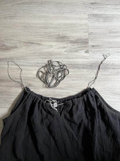 A black cotton nightgown with a drawstring strap of braided grey sashiko thread on a grey wooden floor. Between the straps is the old worn out strap string.