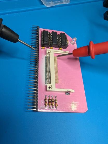 The front side of the pink CF card PCB with the red and black multimeter leads probing pins on the CF interface and the PCB header pins