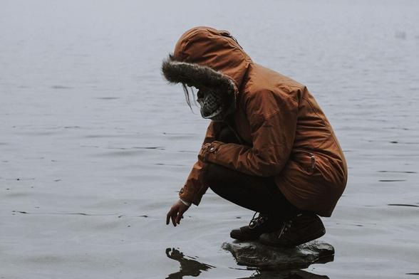 A refugee child kneels on a sea shore
