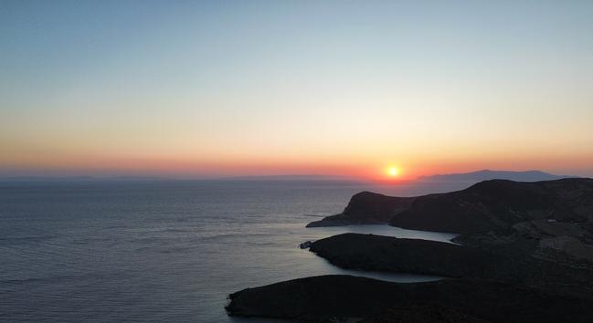 Photo of the sunset. Photo taken from the northern part of the island of Syros, Greece. The mountainous coastline of the island appears dark. The sea is calm and the sun is setting in the horizon. In the horizon three other islands are somewhat visible in the distance (most likely Kea, Kythnos and Serifos), and the sun is setting between two of them.