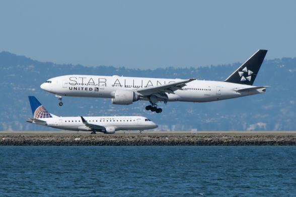 A larger airplane about to touch down, seemingly landing on top of a smaller plane taxiing in the opposite direction.