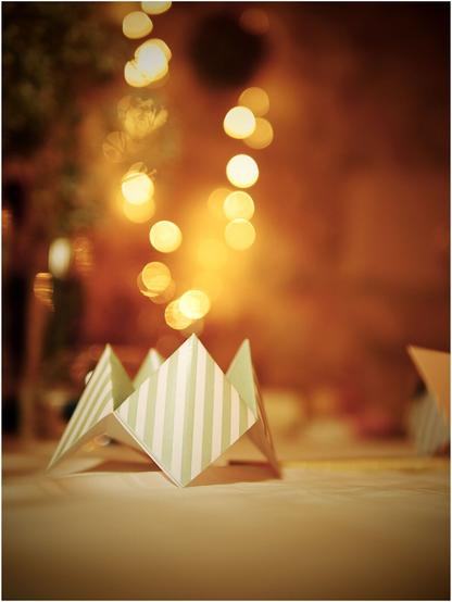 Sur une table, une cocotte en papier sert de décoration.
Des lumières (guirlande lumineuse), en arrière-plan, floues, forment un bokeh. Elles donnent l'impression de flammes qui s'élèveraient de la cocote.