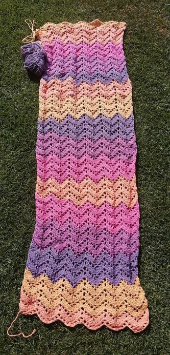 A crocheted scarf with a wave-y pattern and colored stripes from yellow to orange to pink to purple to violet and again.
