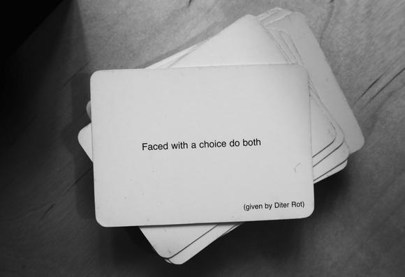 A black-and-white photo of an Oblique Strategy card. The card reads: 'Faced with a choice, do both (given by Dieter Rot)'.