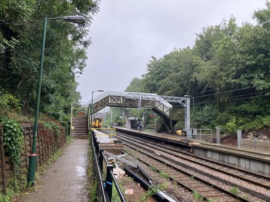 A long view of a railway station. A train is departing. A footbridge crosses the tracks.