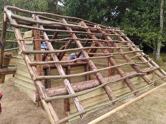 Ein Holzhaus mit Zeltdach, durch die  Dachlatten kann man noch hindurch sehen