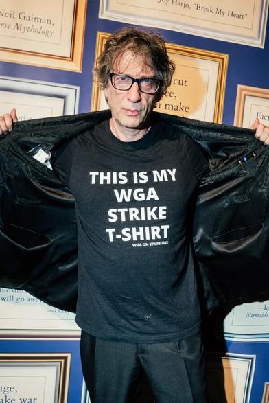 “Neil Gaiman, a best-selling author whose works have frequently been adapted for the screen, in his natural mode: a black T-shirt [that says ‘this is my WGA strike t-shirt’]. Credit...Jutharat Pinyodoonyachet for The New York Times”