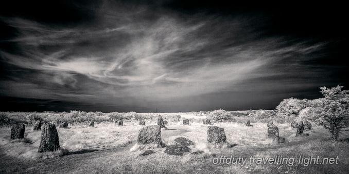 Black and white infrared photo of a stone circle in a grassy area and a dark sky with wispy clouds.
