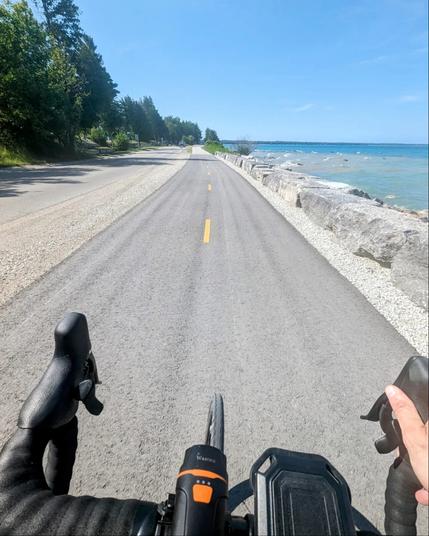 A POV photo of me riding my bike along a paved path, with the blue waters of Lake Huron on the right hand side.