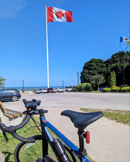 A photo of my bike in front of a giant Canadian flag, with the blue waters of Lake Huron in the background.