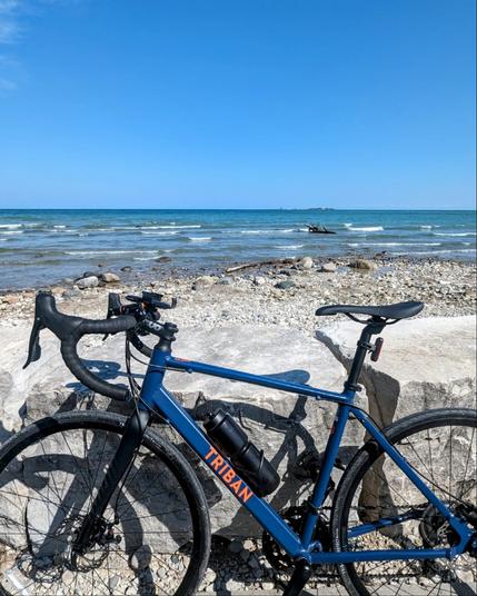 A photo of my bike leaning against some rocks, with a rocky beach and Lake Huron in the background.