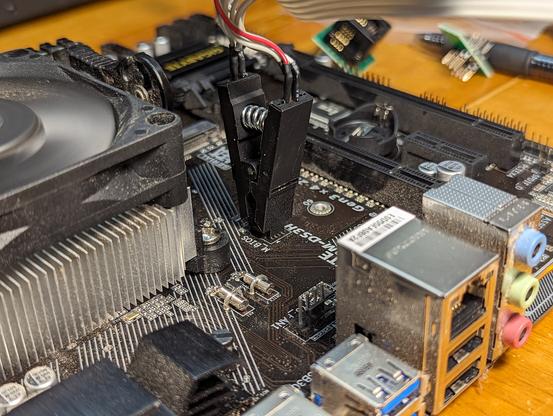 A close-up of the spring clip attached to the BIOS flash chip on the motherboard. There's a light coating of dust on many surfaces. Ignore that.