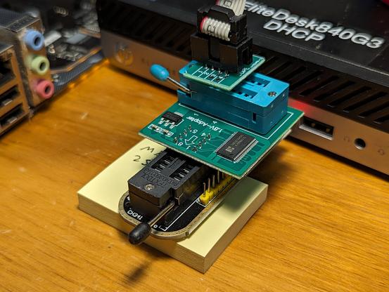 A close-up of the USB programmer, the 1.8v adapter board, and the adapter to the ribbon cable. There's a small pad of sticky notes wedged under it so it doesn't put unnecessary strain on the USB connector.