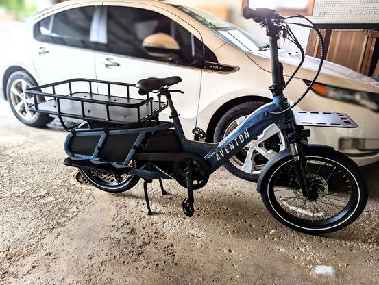 A blue colored Aventon Abound electric bicycle with a rear large metal  basket  and front mounting tray.