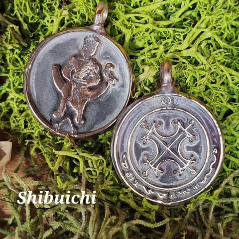 Image of a shibuichi solar talisman showing both the front and back. On the left is the obverse image, with a crowned figure sitting on a throne over a magical symbol, with a raven sitting at his left hand. On the right is the reverse image, with the Agrippan Grand Seal of the Sun in the center and the characters of the sun in an arc along the bottom.