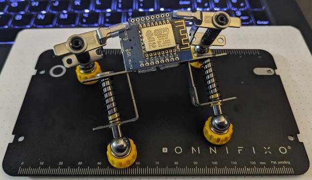 An Omnifixo magnetic "Third Hand" assistant for holding items while working on them for soldering, gluing, painting, etc.
The four "hands" have large parallel jaws held closed by springs. They have a round bottom that rests in a magnet base attached to a metal baseplate.
In this photo, two of the hands are holding a small circuit board and two are holding a row of pins in position to be soldered.