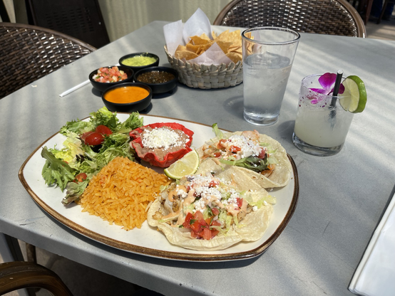 large plate with a fish and shrimp soft taco, a mound of rice, a cup of refried beans and a green salad.