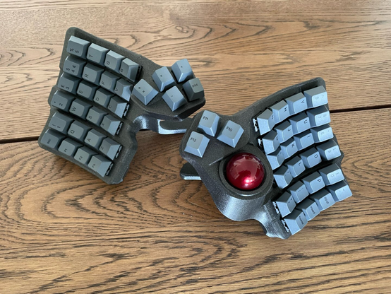 A photograph of a Charybdis keyboard, printed in Prusament Galaxy Black, with grey keycaps and a red trackball.