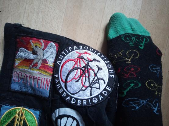 Meine Radfahrsocken mit Fahrrädern drauf in meinem rechten Fuß, dazu ein Stück meiner benähten Kutte. Man sieht einen Aufnäher von Led Zeppelin und "Antifaschistische Fahrradbrigade".