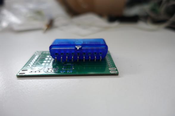 A playstation 2 controller port, lying on top of a leftover pcb. The port has pins bent at a 90 degree angle, but they aren't long enough to reach the surface, instead they are hovering roughly 2mm above it.