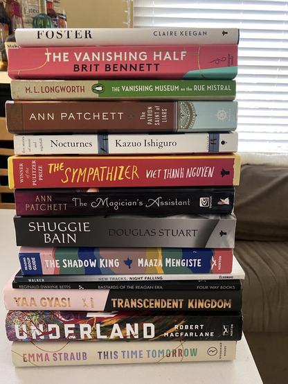 A stack of books piled horizontally on a table with these titles: FOSTER by CLAIRE KEEGAN, THE VANISHING HALF by BRIT BENNETT, THE VANISHING MUSEUM on the RUE MISTRAL by M. L. LONGWORTH, The PATRON SAINT of LIARS by ANN PATCHETT, FIVE STORIES, Nocturnes by Kazuo Ishiguro, THE SYMPATHIZER by VET THANE NGUYEN, The Magician's Assistant by ANN PATCHETT, SHUGGIE BAIN by DOUGLAS STUART, THE SHADOW KING by MAAZA MENGISTE, New Tracks, Night Falling by WALKER, BASTARDS OF THE REAGAN ERA by REGINALD DWAYNE BETTS, TRANSCENDENT KINGDOM by YAA GYASI, Underland by ROBERT MACFARLANE,
THIS TIME TOMORROW by EMMA STRAUB