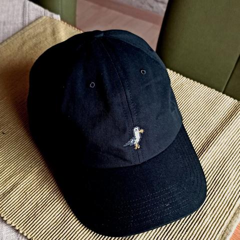 Bild von einer auf einem Tisch liegenden schwarzen Cap mit einer Möwe im 8Bit-Stil als Stickmuster.