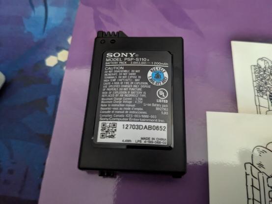 Black Sony PSP battery laying by itself, with a barely noticeable bulge to its shape.