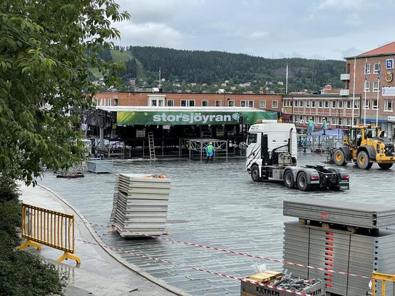 Stortorget i Östersund. Festivalen Storsjöyrans stora scen byggs upp inför fredag och lördag. En lastbil och baklastare syns.