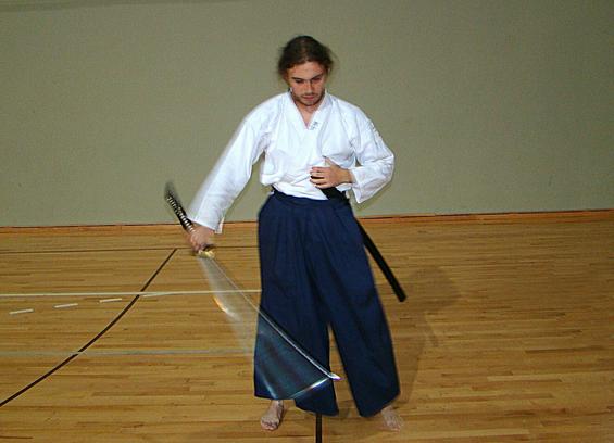 Longhaired man in white gi and blue hakama performing chidori.