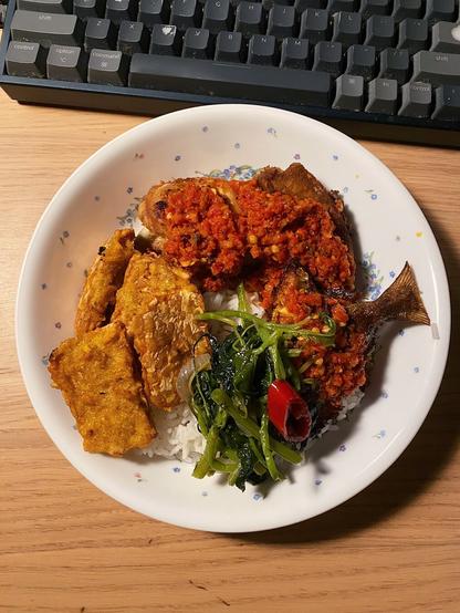 White rice in a ceramic plate, served with Ayam Goreng (fried chicken) and Ikan Goreng (fried fish) both generously covered with Sambal Balado, Tempe Goreng, and Sayur Bayam (Amaranth).