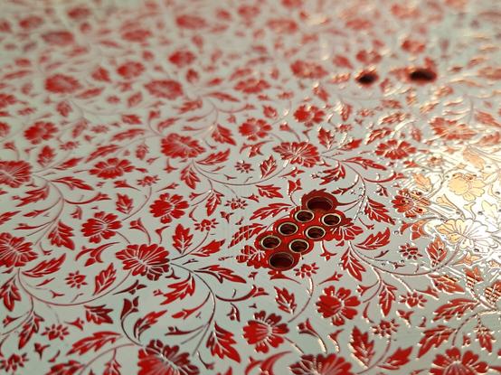 A footprint for a 6-pin direct-to-board connector surrounded by a floral silkscreen pattern. Thee pattern consists of stylized chrysantemum flowers and leafy vines. The connector footprint has six large plated holes with narrow annular rings in a staggered two-row arrangement, flanked by two larger non-plated guiding holes.
