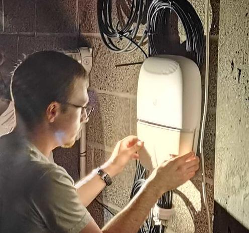 Photo of myself working by flashlight to replace the protective panel of a Ubiquiti (EP-S16) EdgePoint S16 outdoor PoE switch after crimping and installing a cable to the CubePro.