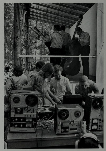 men in button-down shirts tend to reel-to-reel tape recorders while bluegrass band plays onstage