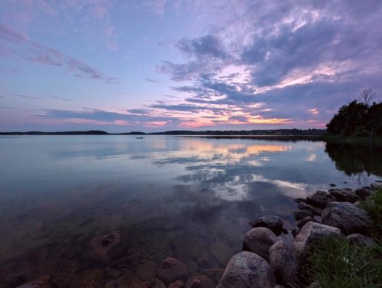 A soft purple sunset over a reflective, calm lake.