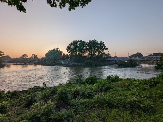 The sun is setting over a river surrounded by greenery.
