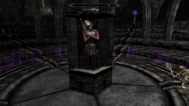 In a crypt deep underground, surrounded by pillars and arches, rests a vampire woman dressed in red and black, with an Elder Scroll strapped to her back.