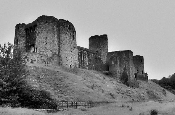 A ruined but still imposing Kidwelly Castle overlooks any approaching visitor. Pictured in monochrome to enhance the atmosphere.