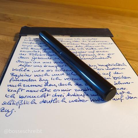 A Black fountain pen lying on a notepad with blue writing on it