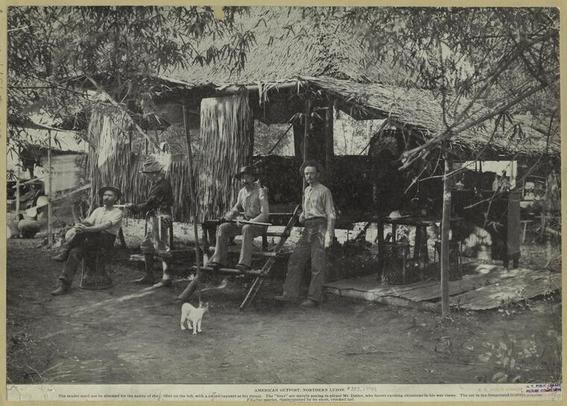 a group of men pictured in front of a small hut