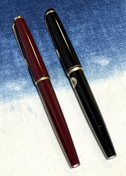 Two capped fountain pens, left is burgundy, right is black, both with gold trim