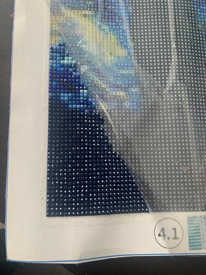 a photo of a work in progress diamond art with a corner of the canvas covered in little coloured square crystals