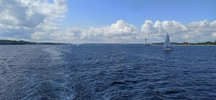 Die kieler Förde mit vielen Booten und einen grün weißen Leuchtturm. Es ist sonnig und das Bild auf dem Wasser entstanden.