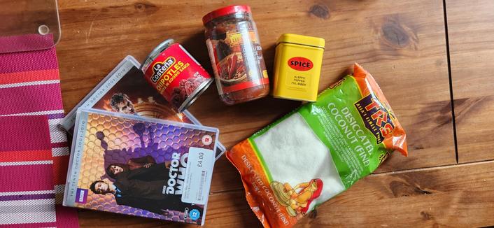 Posés sur une table, la saison 4 de Doctor Who en DVD, une conserve de piments Chipotle en adobo, un bocal de doubajang, du piment d'alep, de la noix de coco séchée.