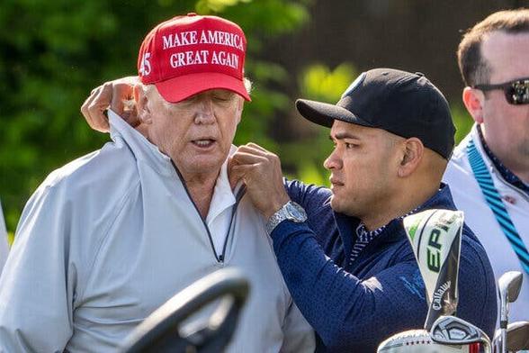 Trump and his assistant Walt Nauta, on a golf course. Nauta is carefully adjusting the collar on Trump’s pullover/fleece.