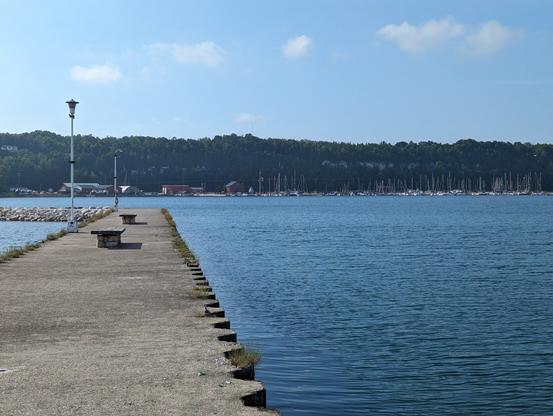 A cement pier on Georgian Bay with an escarpment and sailboats in the distance. It is sunny, and the water is a deep blue.