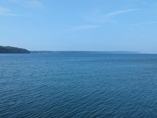 A bright sunny day with a vast view of the blue Georgian Bay waters. There is an escarpment in the distance, and a slight haze covering it.